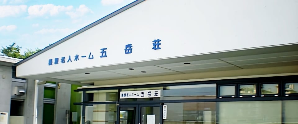 介護施設の建物外観。白い壁に青い施設名の看板が掲げられている。
